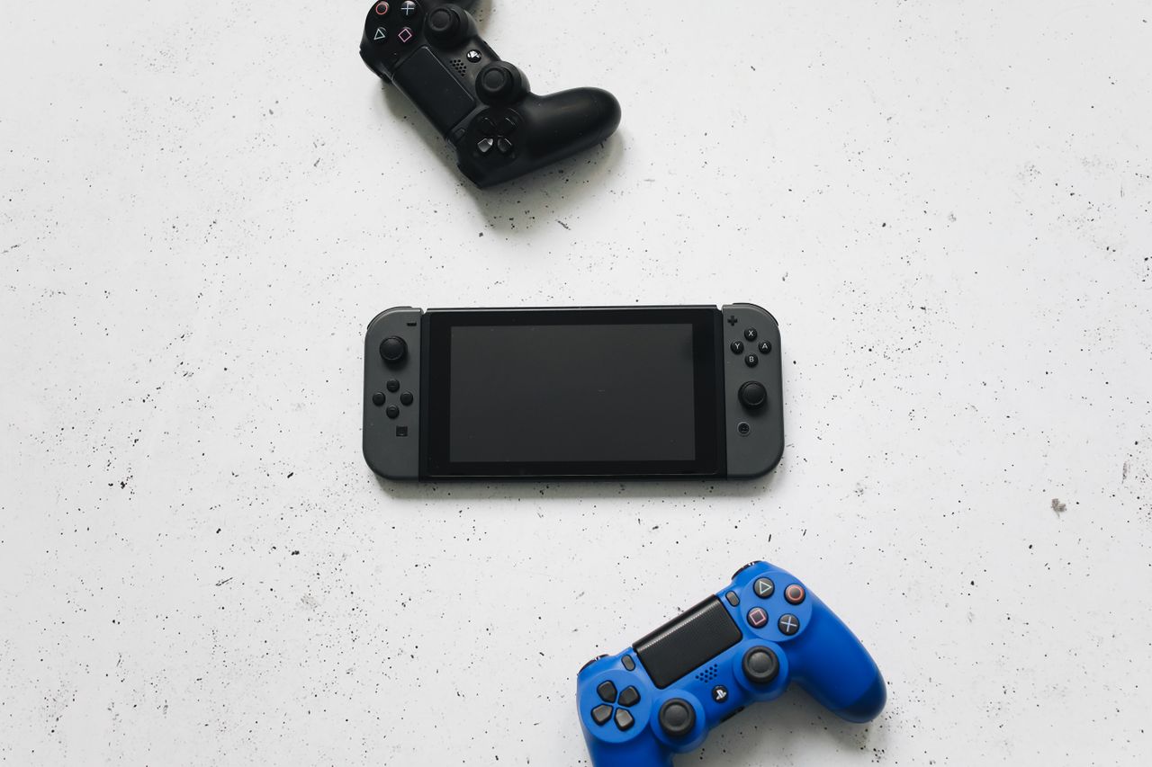 Flat lay of gaming consoles and controllers on white surface, featuring popular gaming devices.
