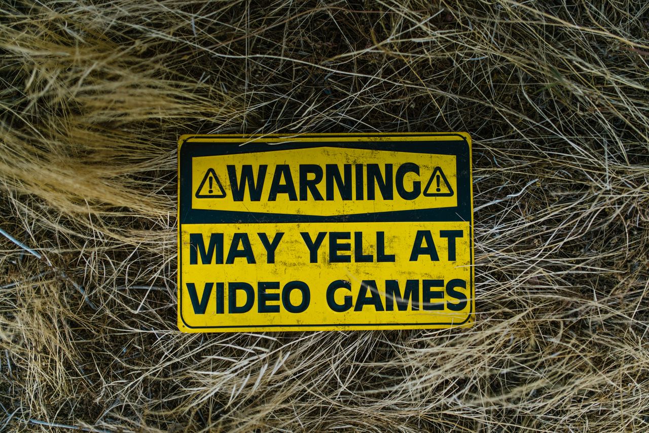 A funny yellow warning sign on grass reading 'Warning May Yell at Video Games'.